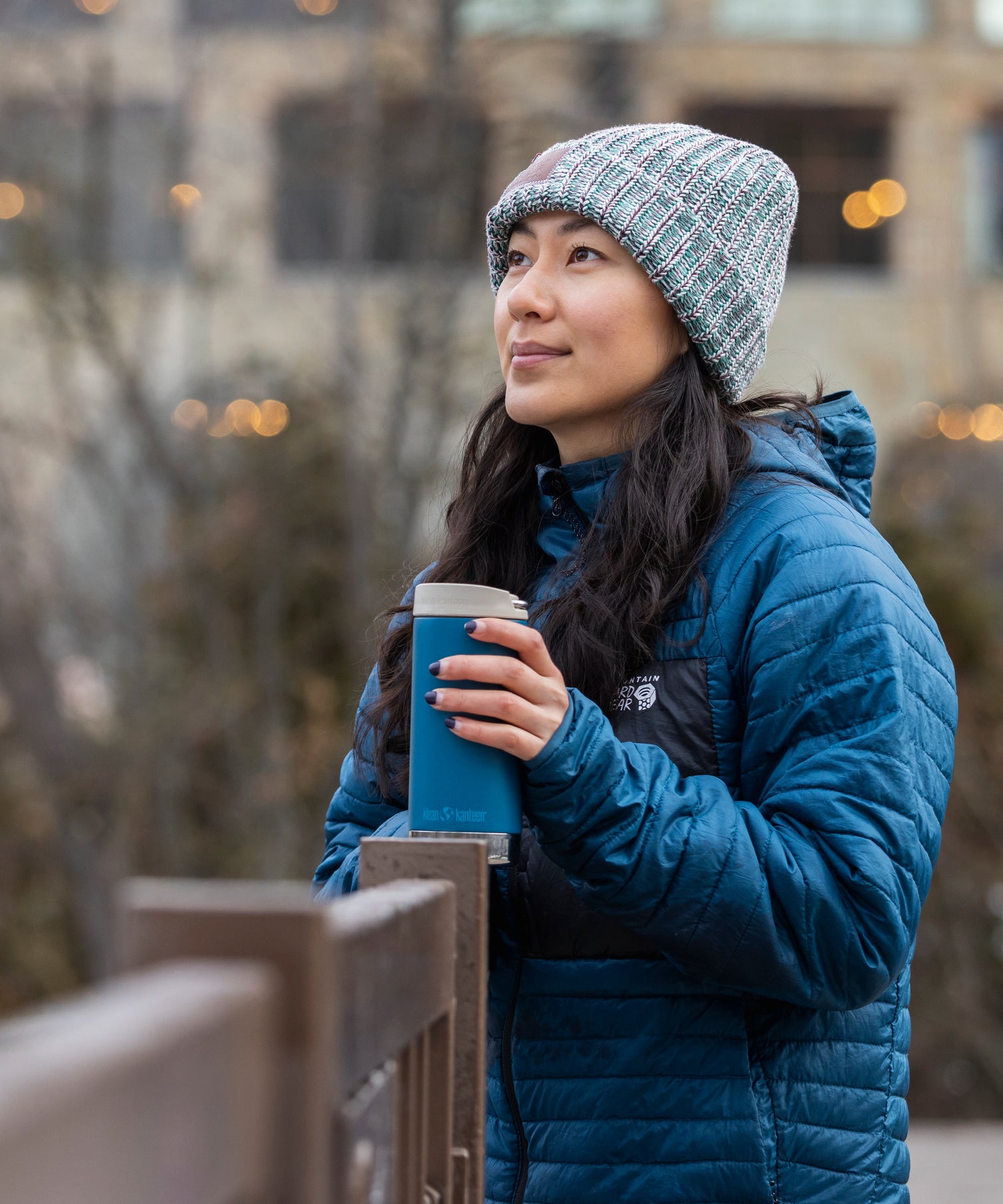 A person looking into the distance whilst holding a Klean Kanteen 12oz TKWide Cafe in the corsair colour on a wooden fence.