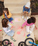 4 children sitting on a concreate path drawing with chalks, four different Kid Kanteen can be seen. One child is drinking out of a mushroom print sippy cap Kid Kanteen. There are 3 other Kid Kanteen on the ground next to the children, an insulated Ice Cream print bottle, an insulated Mountain Range bottle and a Milky Way print bottle.