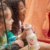 Two children on a swing, one child is holding a Kid Kanteen 12oz Narrow Sippy Bottle featuring a leaping unicorns print.