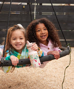 Two children on a circular swing, one child has a unicorn print Kid Kanteen 12oz Narrow Sippy Bottle.