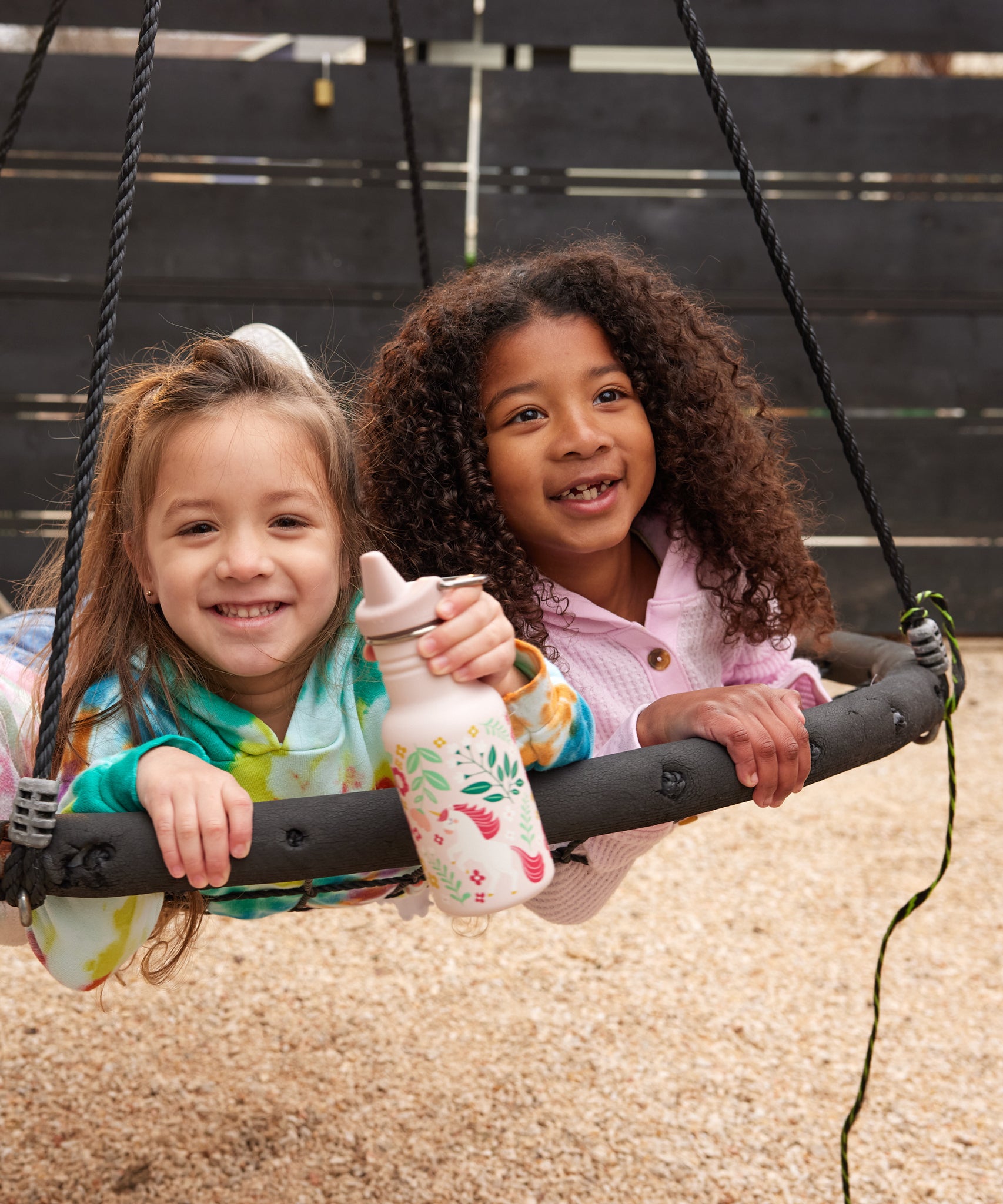 Two children on a circular swing, one child has a unicorn print Kid Kanteen 12oz Narrow Sippy Bottle.