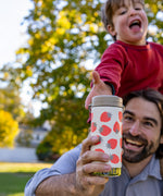 A child reaching for a Klean Kanteen 12oz Tofu Strawberries Print TKWide from an adult. The child is sitting on the adult's shoulders.