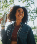 A woman standing under a tree and holding a opened klean Kanteen 16oz reflect stainless steel rise bottle