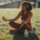 A woman doing yoga outside on grass next to a klean Kanteen 16oz reflect stainless steel  insulated bottle