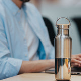 A man sitting in a office environment  with the  klean Kanteen 16oz reflect stainless steel rise bottle on a wooden table