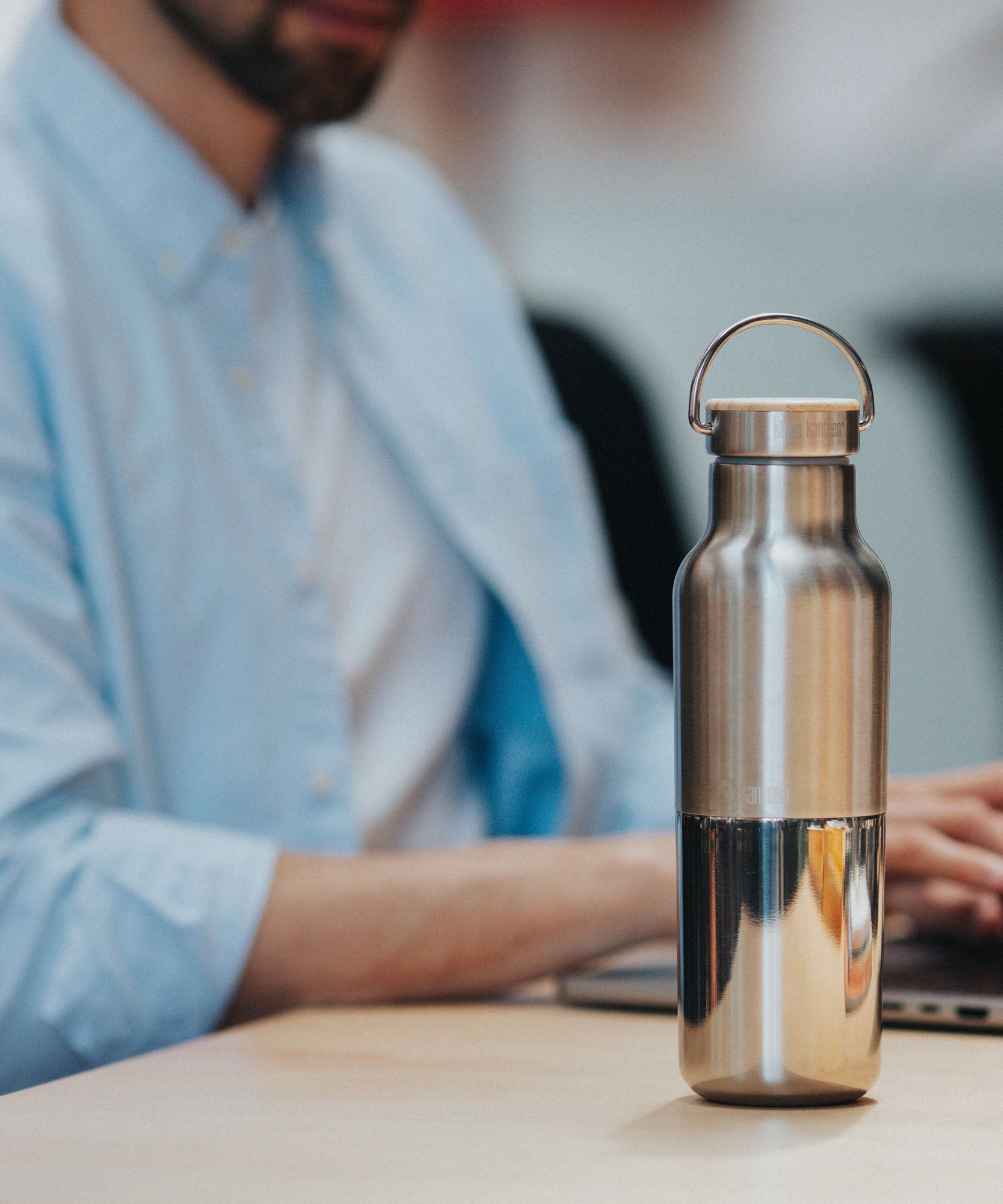 A man sitting in a office environment  with the  klean Kanteen 16oz reflect stainless steel rise bottle on a wooden table