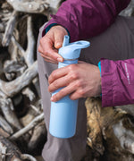 A close up of a person's hand holding a Clear Sky coloured Klean Kanteen 18oz Classic Narrow Leakproof Flip Seal Sports Cap Reusable Stainless Steel Water Bottle.