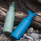 Two Klean Kanteen 18oz Classic Narrow Flip Seal Sports Cap Reusable Stainless Steel Water Bottle resting on stones and driftwood. One bottle is in the Sea Spray green colour and the other is the Corsair blue colour.