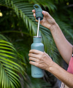 A close up of a person's hand holding a Sea Spray coloured Klean Kanteen 18oz Classic Narrow Flip Seal Sports Cap Reusable Stainless Steel Water Bottle. They have taken the lid off revealing the stainless steel straw attached to the lid.