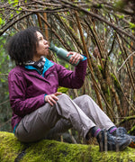 A person sitting on a moss covered surface drinking from a Sea Spray green coloured Klean Kanteen 18oz Classic Narrow Flip Seal Sports Cap Reusable Stainless Steel Water Bottle.