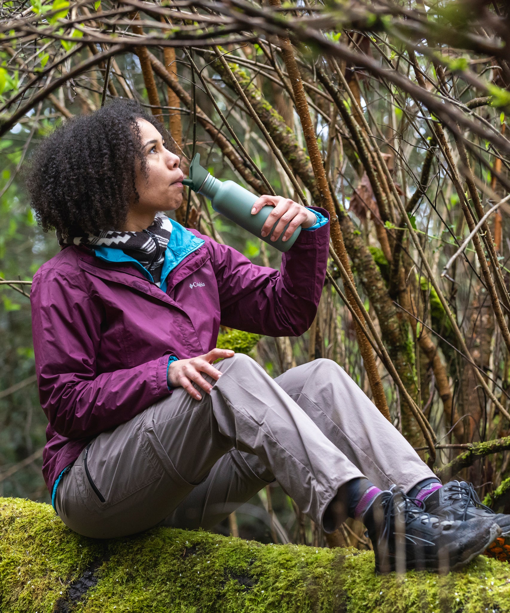 A person sitting on a moss covered surface drinking from a Sea Spray green coloured Klean Kanteen 18oz Classic Narrow Flip Seal Sports Cap Reusable Stainless Steel Water Bottle.
