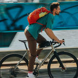 A man on a bike cycling with the acacia Klean Kanteen 20oz classic rise bottle in a bottle holder on a bag. A Reusable Stainless Steel Water Bottle with loop cap