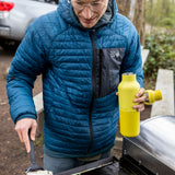 A man cooking outside and holding the Acacia 20oz rise Klean Kanteen water bottle with the loop cap off the bottle