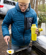 A man cooking outside and holding the Acacia 20oz rise Klean Kanteen water bottle with the loop cap off the bottle
