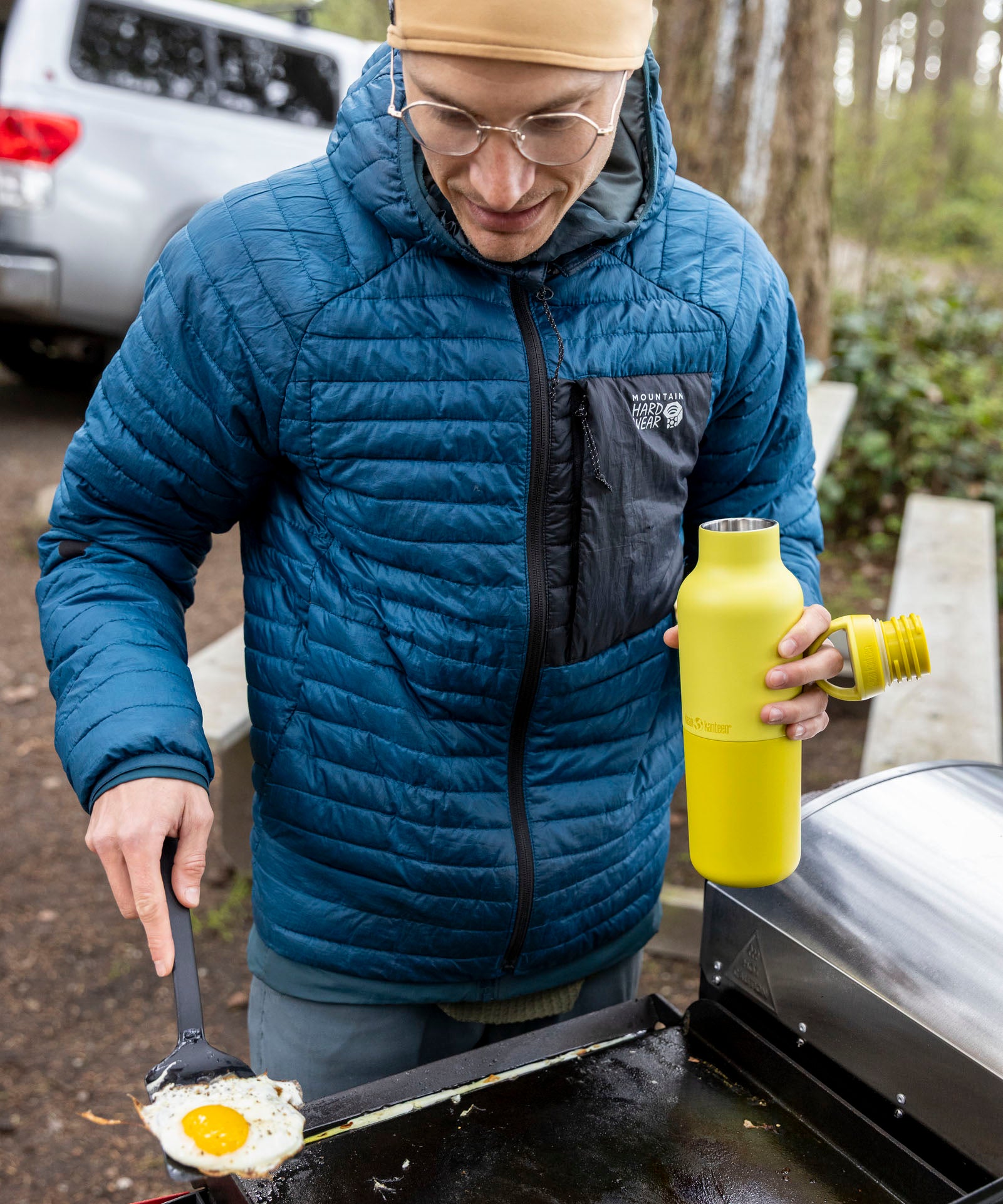 A man cooking outside and holding the Acacia 20oz rise Klean Kanteen water bottle with the loop cap off the bottle