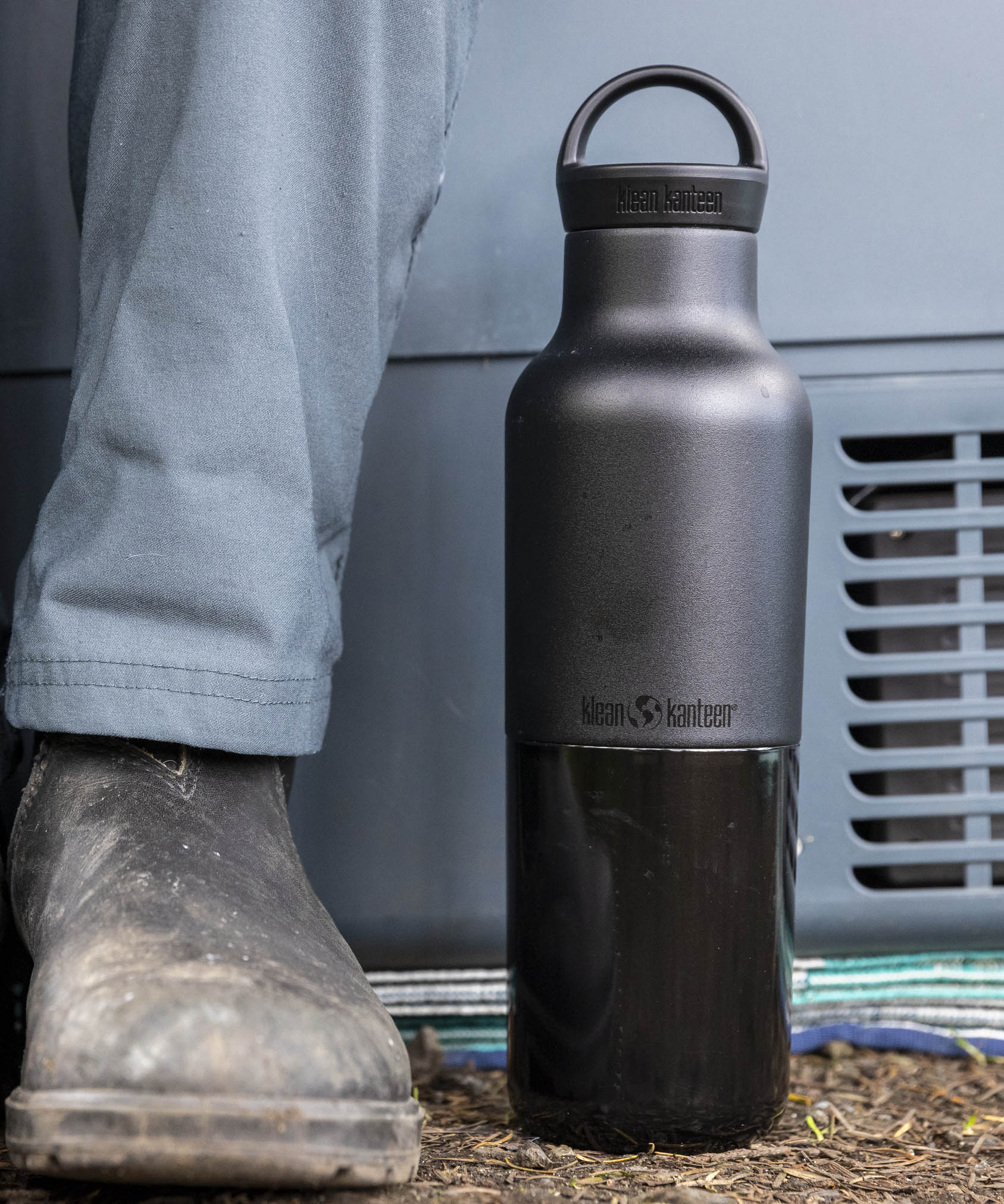 A close up of the black 20oz Klean Kanteen Reusable Stainless Steel Water Bottle next to a adult leg showing the size and coating detail