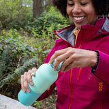 A woman sitting by the woodsand closing the loop cap on the Klean Kanteen 20oz cabbage rise bottle