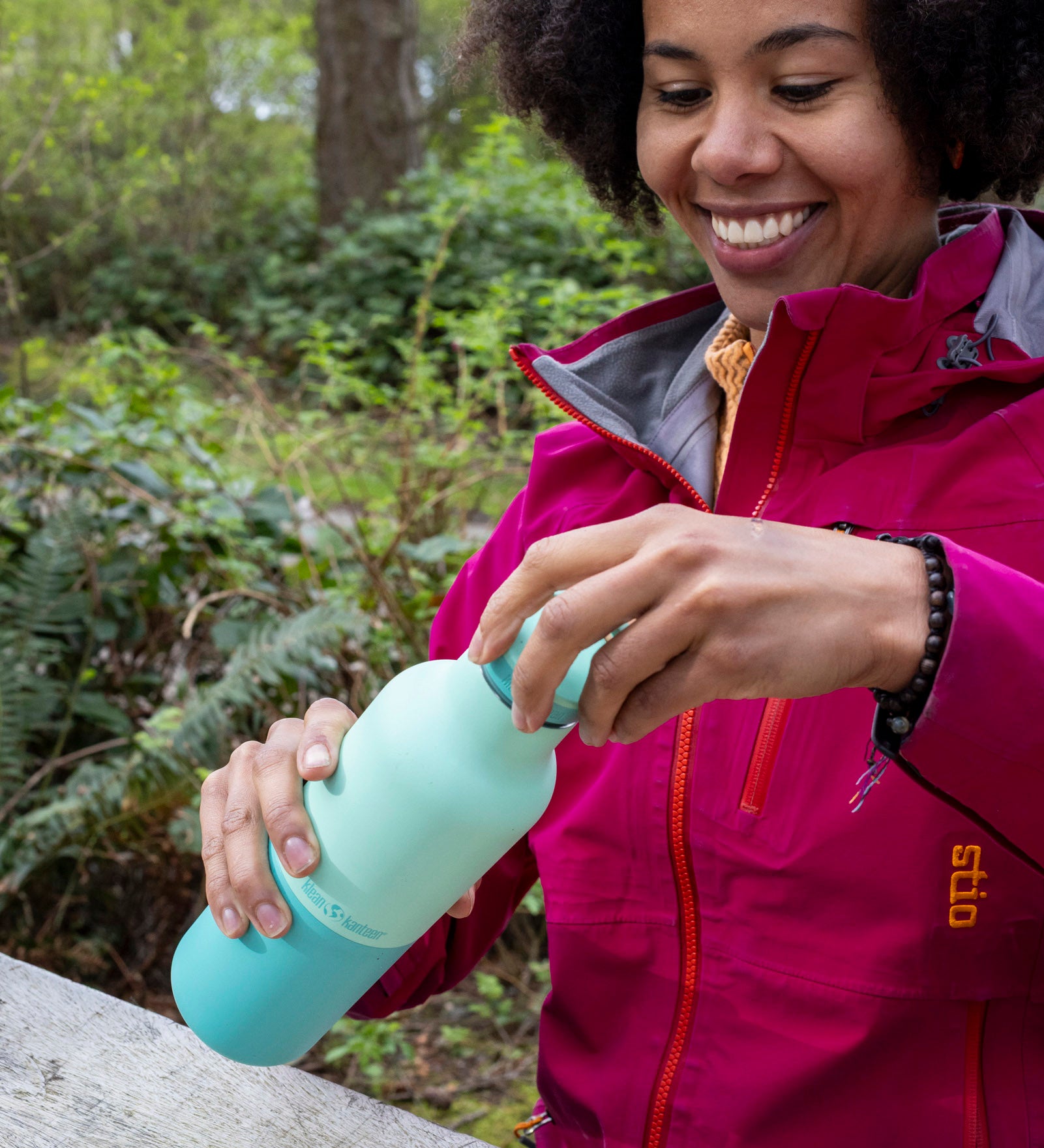 A woman sitting by the woodsand closing the loop cap on the Klean Kanteen 20oz cabbage rise bottle