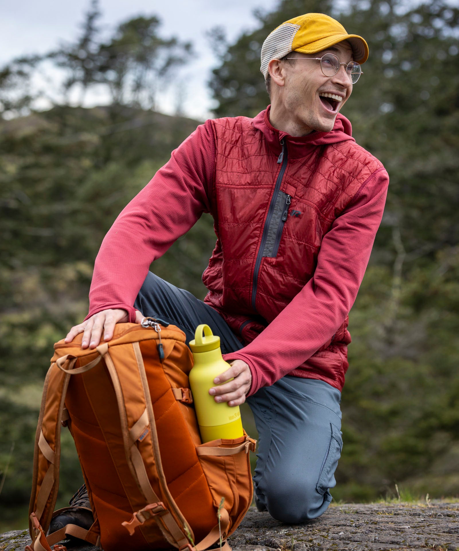 A man reaching out for a acacia 20oz Klean Kanteen rise Reusable Stainless Steel Water Bottle from a holder on a backpack