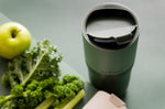 Close up of the flip lid on the Klean Kanteen stainless steel insulated drinks tumbler on a dark green background next to an apple