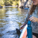 A person on the water holding a Corsair blue coloured Klean Kanteen 27oz Classic Narrow Flip Seal Sports Cap Reusable Stainless Steel Water Bottle in their hand.