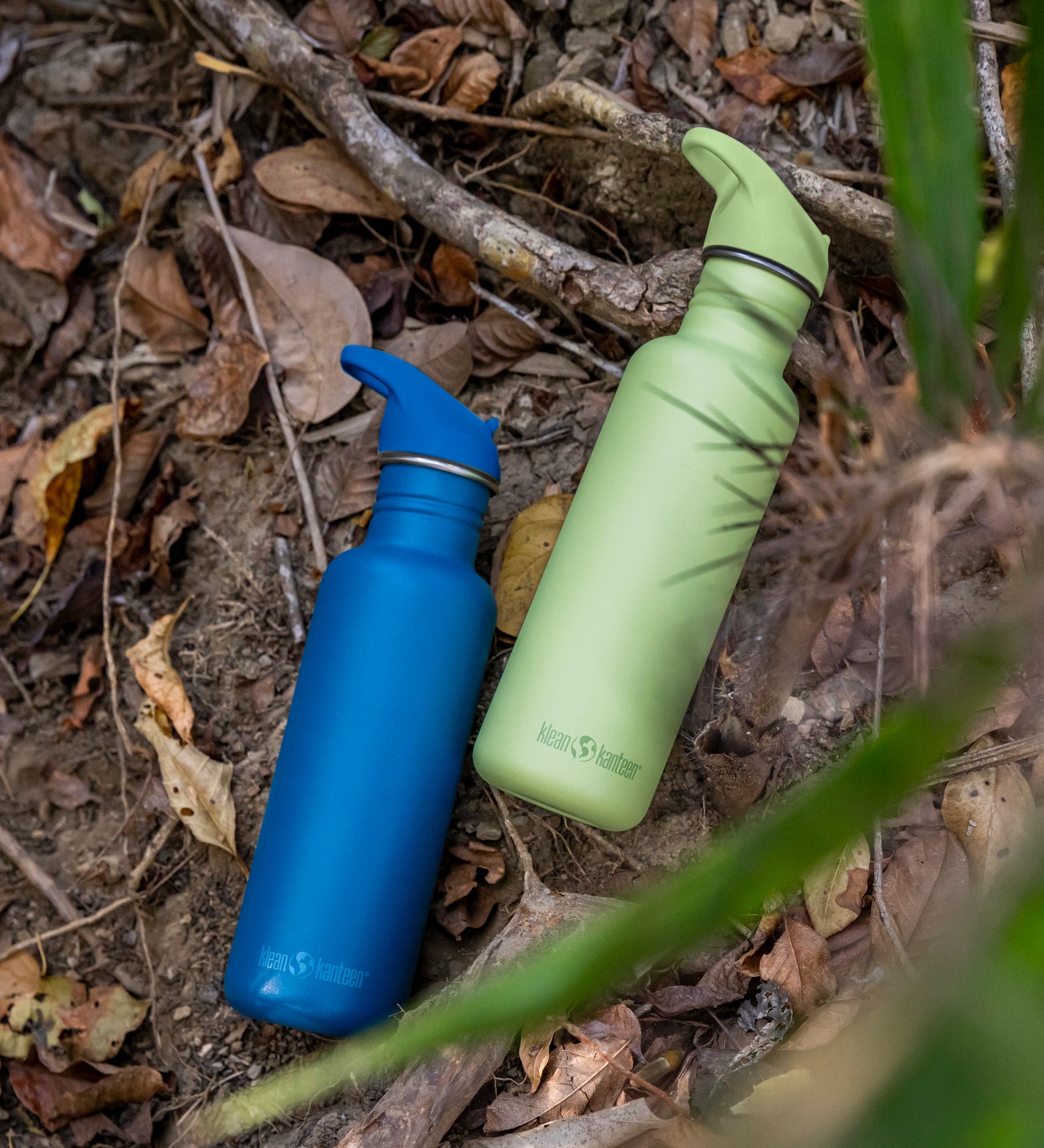 Two corsair blue and shadow lime coloured Klean Kanteen 27oz Classic Narrow Leakproof Flip Seal Sports Cap Reusable Stainless Steel Water Bottle laying on the ground.