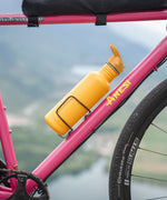 A Sunset yellow coloured Klean Kanteen 27oz Classic Narrow Flip Seal Sports Cap Reusable Stainless Steel Water Bottle placed in a bottle holder of a pink coloured bike. .