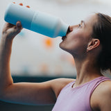 A woman drinking from the the 20oz barely blue stainless steel reusable Klean Kanteen bottle