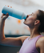A woman drinking from the the 20oz barely blue stainless steel reusable Klean Kanteen bottle