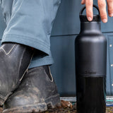 A close up of a adult hand reaching down to a black 20oz Klean Kanteen Reusable Stainless Steel Water Bottle available at Babipur