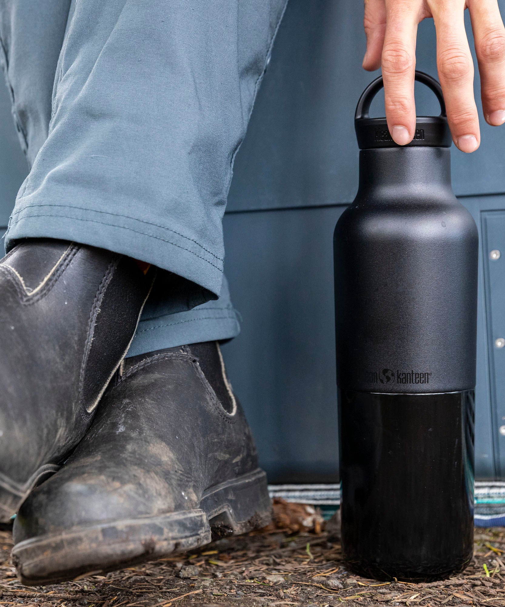 A close up of a adult hand reaching down to a black 20oz Klean Kanteen Reusable Stainless Steel Water Bottle available at Babipur