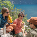 Three hikers enjoying a rest with an amazing view of the sea, drinking from their Klean Kanteens with flip seal sports caps.