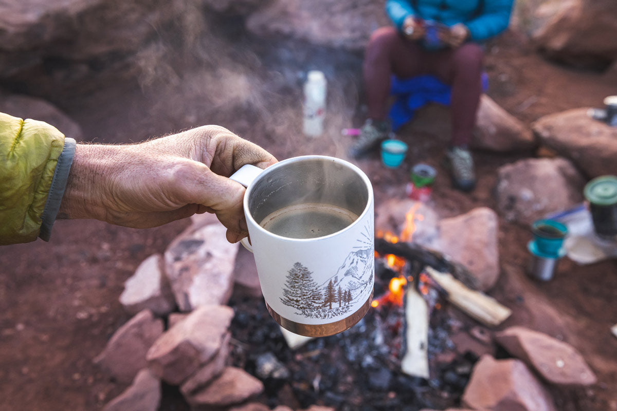 Close up of a hand holding the Klean Kanteen eco-friendly metal travel mug over a camp fire