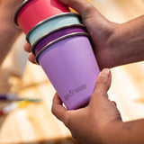 Hands holding a stack of Klean Kanteen stainless steel kid cups 10oz in bright pinks and purples - plastic free, made from post-consumer steel, available to buy at Babipur.