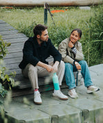 2 adults sitting down and holding the Klean Kanteen reflect stainless steel rise bottles by the handles on the loop cap