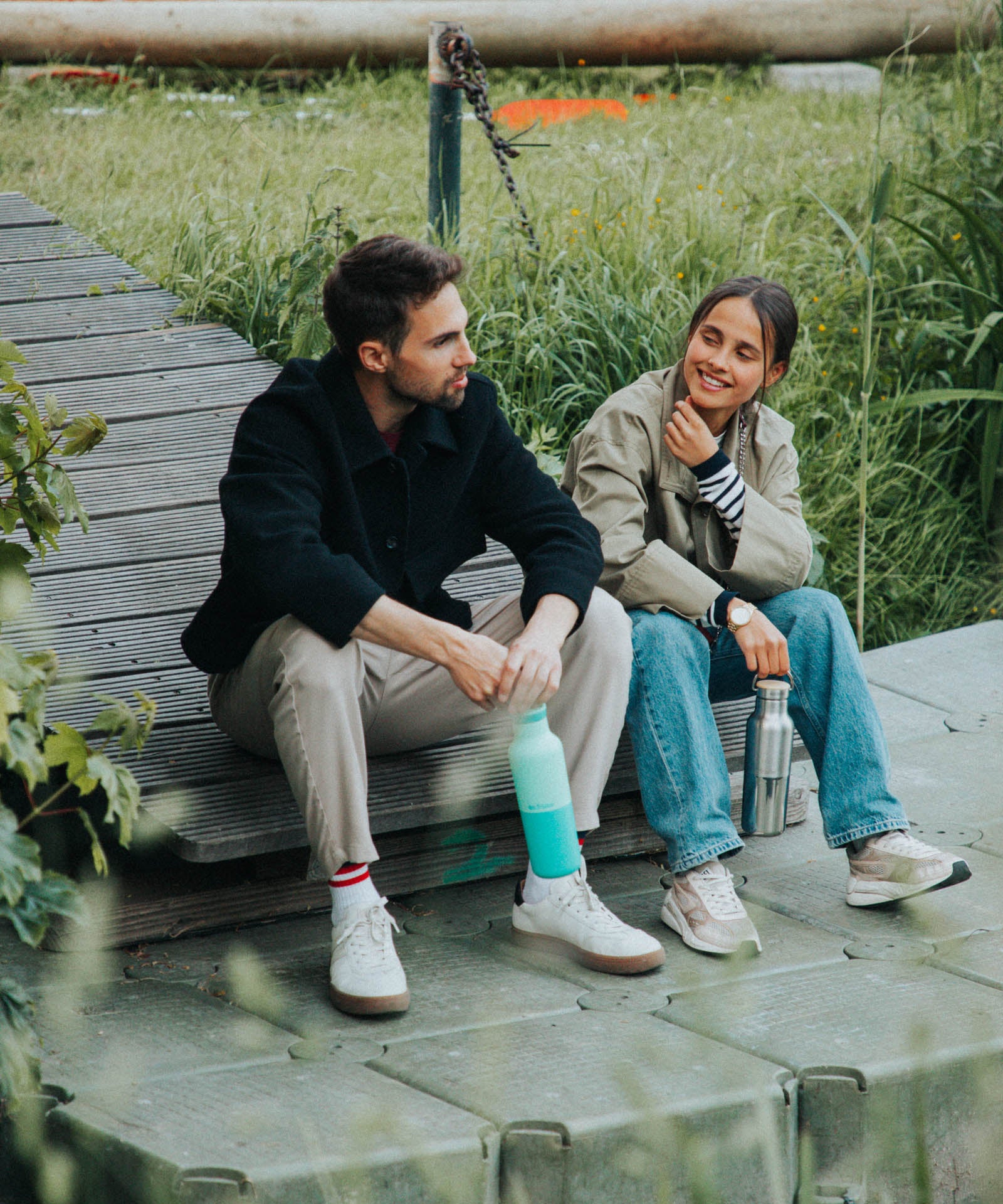 2 adults sitting down and holding the Klean Kanteen reflect stainless steel rise bottles by the handles on the loop cap