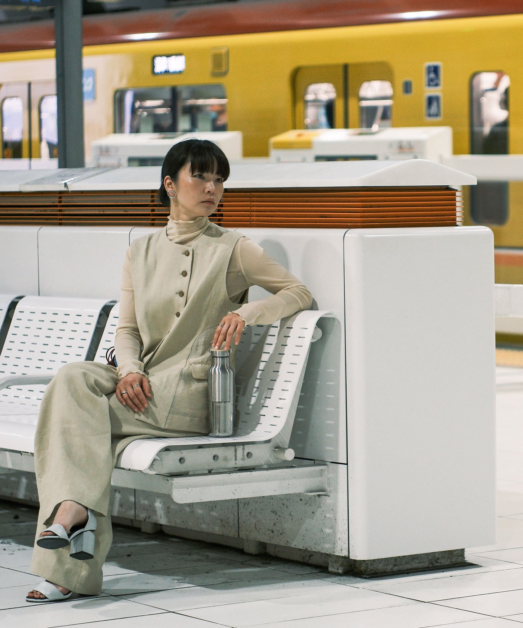 A woman sitting in on a bench in a trainstation and holding the  klean Kanteen reflect stainless steel rise bottle