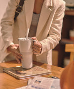 A close up of a person's hands holding a barley blue coloured 26oz handled rise tumbler from Klean Kanteen ready to lift it up off a table.