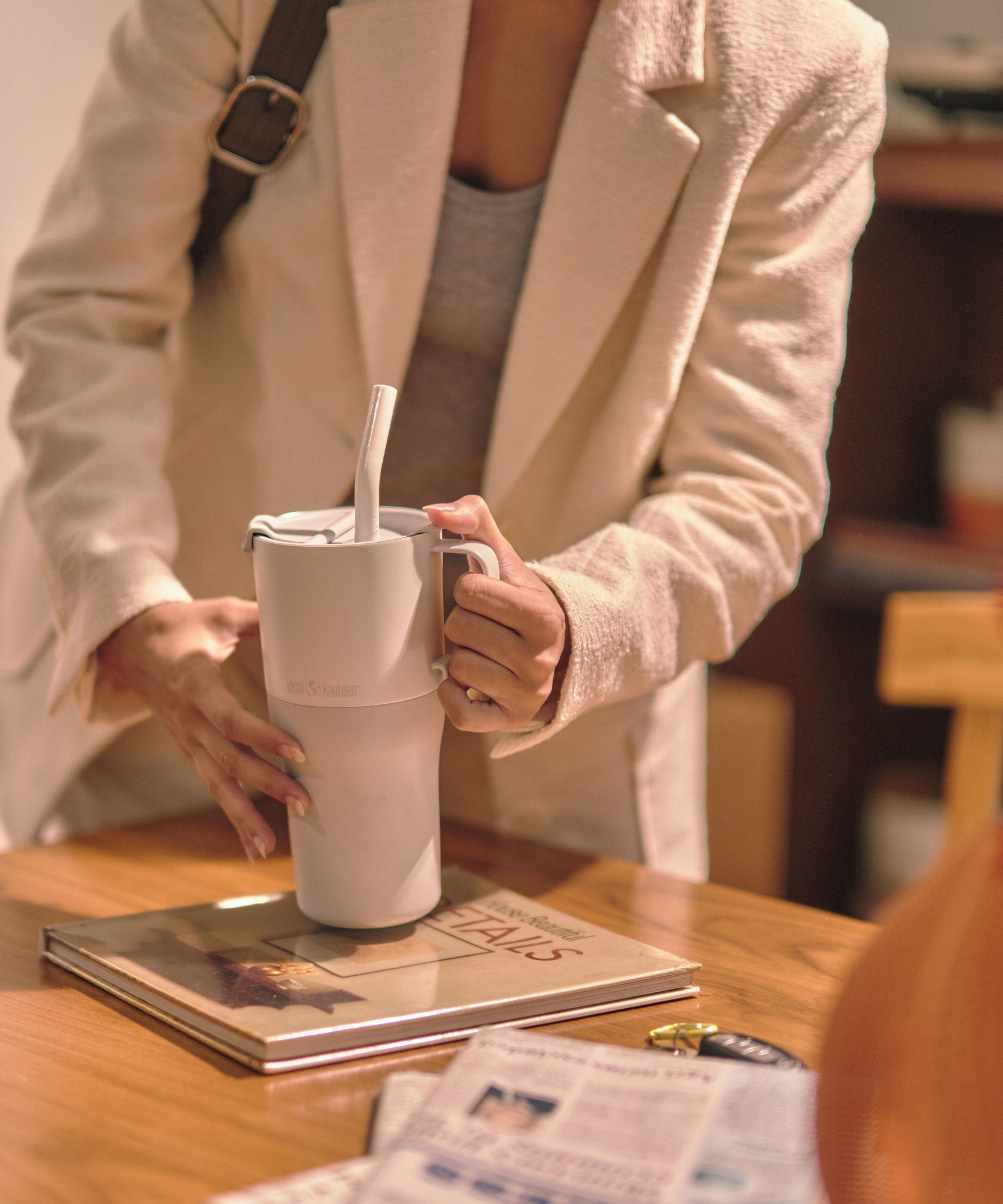 A close up of a person's hands holding a barley blue coloured 26oz handled rise tumbler from Klean Kanteen ready to lift it up off a table.