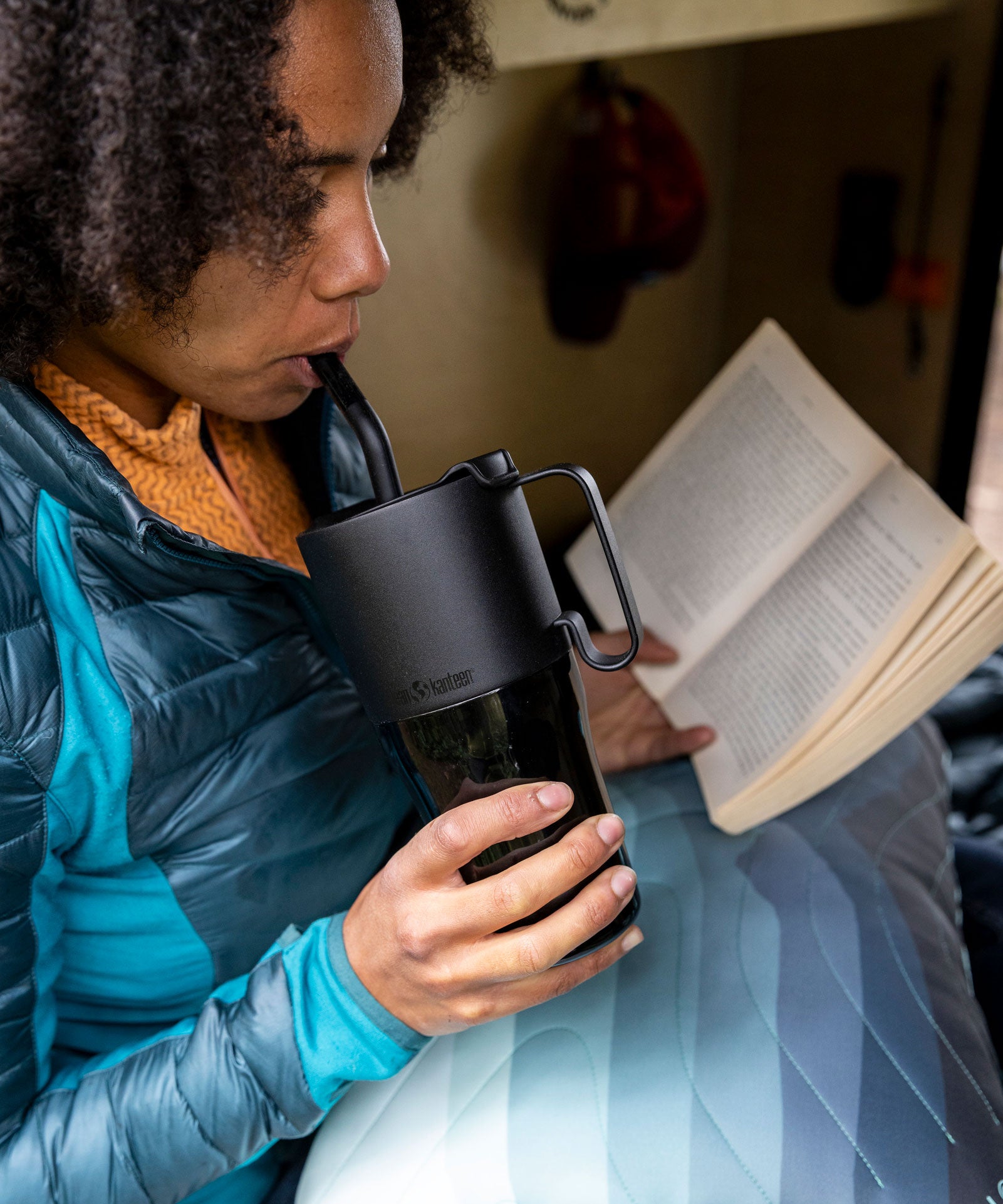 A woman drinking from a black Klean Kanteen 26oz handled Rise Tumbler whilst reading a book.