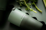 Close up of a Klean Kanteen stainless steel 26oz tumbler on a dark green background next to some green vegetables