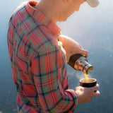 Man crouched down pouring the Klean Kanteen TKPro stainless steel drinks flask next to a stone campfire
