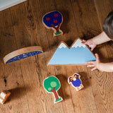 Looking down at a child playing with the Lanka Kade Babipur moel mountain toy and other dan y ser wooden toys on a wooden floor
