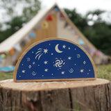 Close up of the Lanka Kade Babipur dan y ser semi circle block toy on a wooden log in front of a beige tent