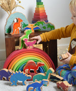 A child reaching for a Lanka Kade caudipteryx pink dinosaur wooden toy figure. These wooden toy figures are part of a huge range of Lanka Kade fair trade, wooden toys available here at Babipur.