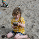 A child playing with Lanka Kade coconut bowls and utensils on the beach.