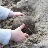 A child placing an upturned Lanka Kade coconut bowl on the sand at a beach.