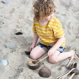 A child playing with Lanka Kade coconut bowls and utensils on the beach.