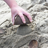 An upturned Lanka Kade coconut bowl being emptied of sand. A dome of sand has been created.