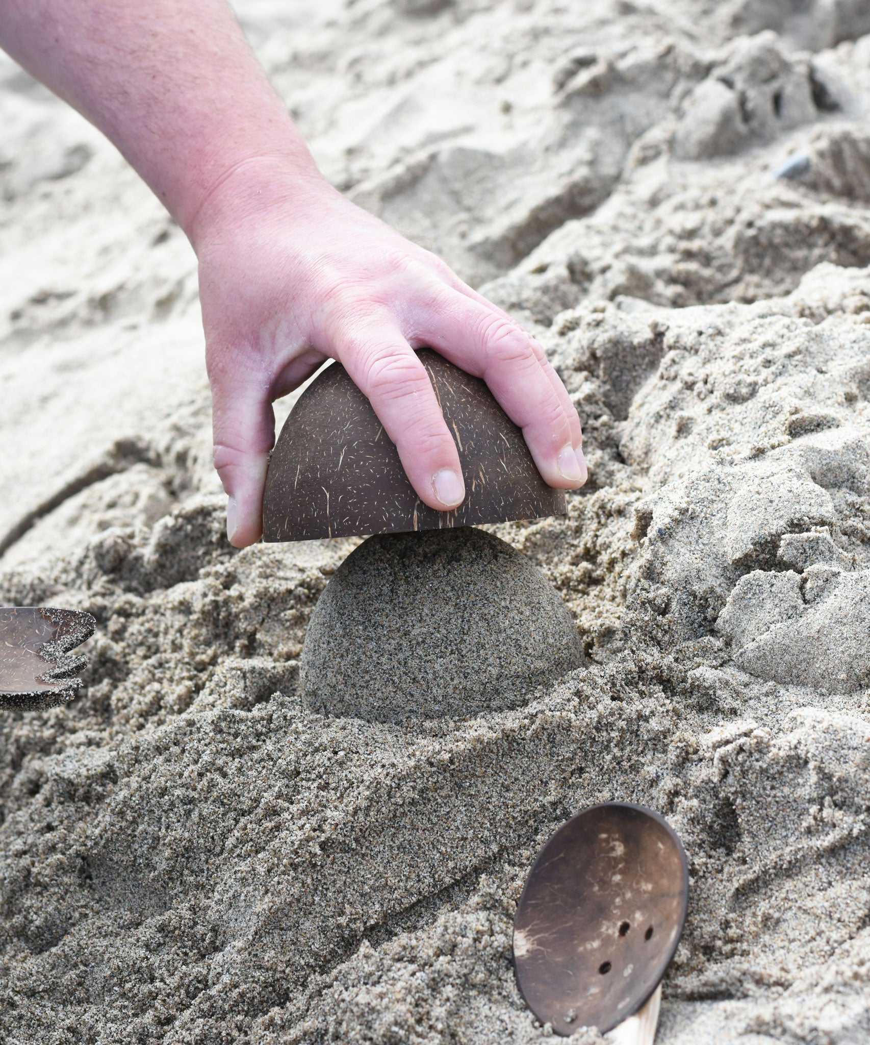 An upturned Lanka Kade coconut bowl being emptied of sand. A dome of sand has been created.